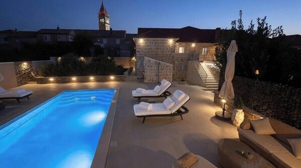 A swimming pool with lounge chairs, a stone staircase, and a view of a tower in the background. - Villa Dalma (Cilipi)