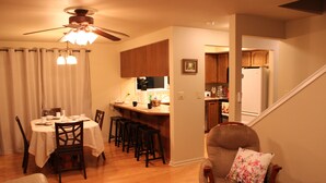 Un espace repas avec une table dressée pour quatre personnes, un coin bar et une cuisine visible à travers une porte ouverte.