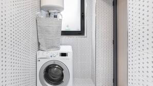 A compact laundry room with a front-loading washing machine, a stacked drying rack, and a window above the machine.