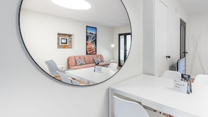 A modern hotel room with a round mirror reflecting a cozy seating area, a white desk, and a door with a sign.