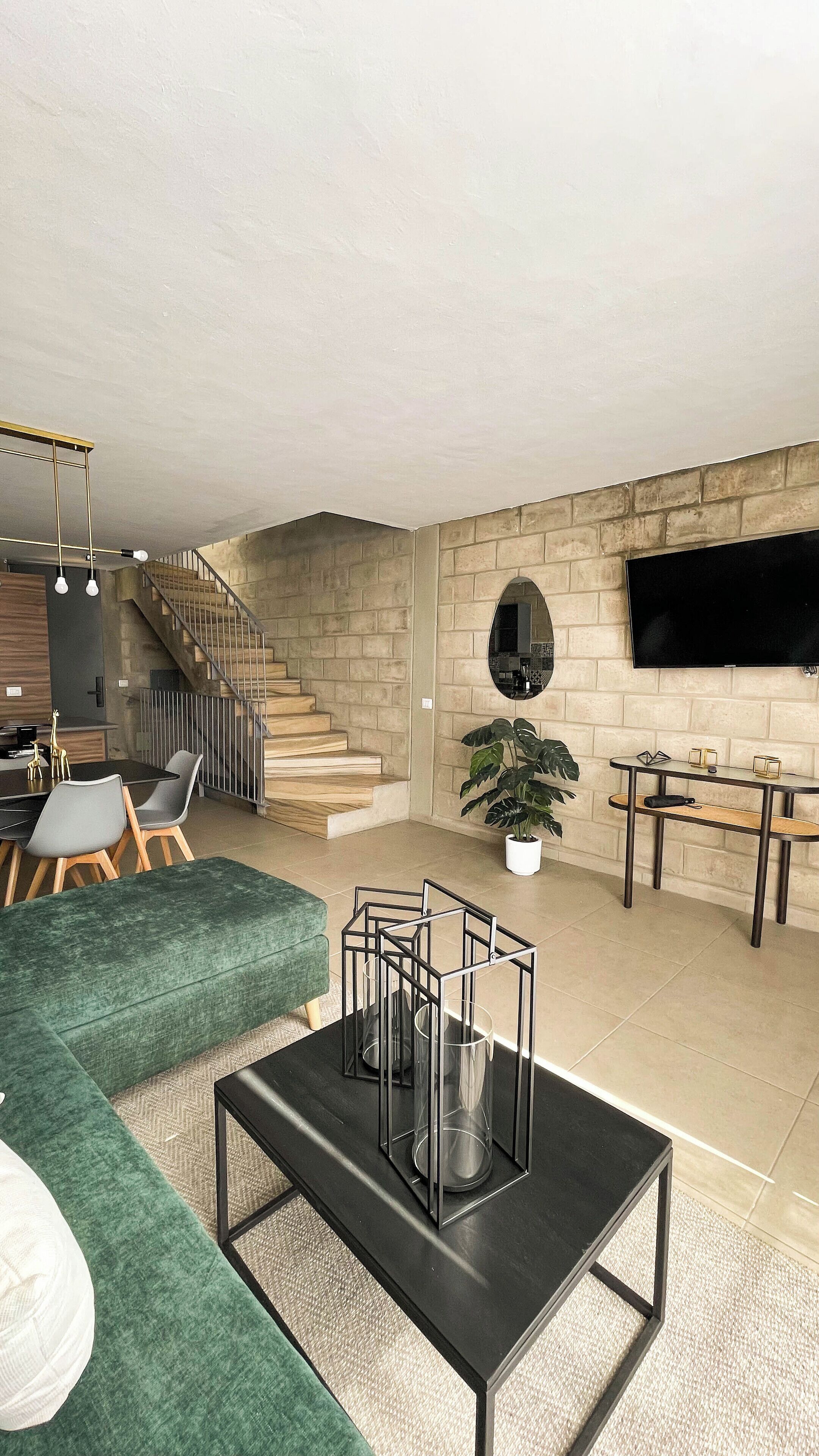 A spacious living area with a staircase, a dining table, and a TV mounted on the wall.