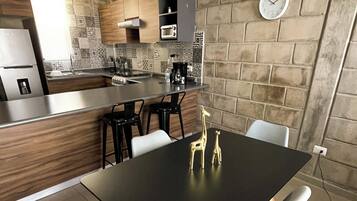 Une cuisine moderne avec une table à manger noire, des chaises blanches et une sculpture décorative représentant une girafe dorée.