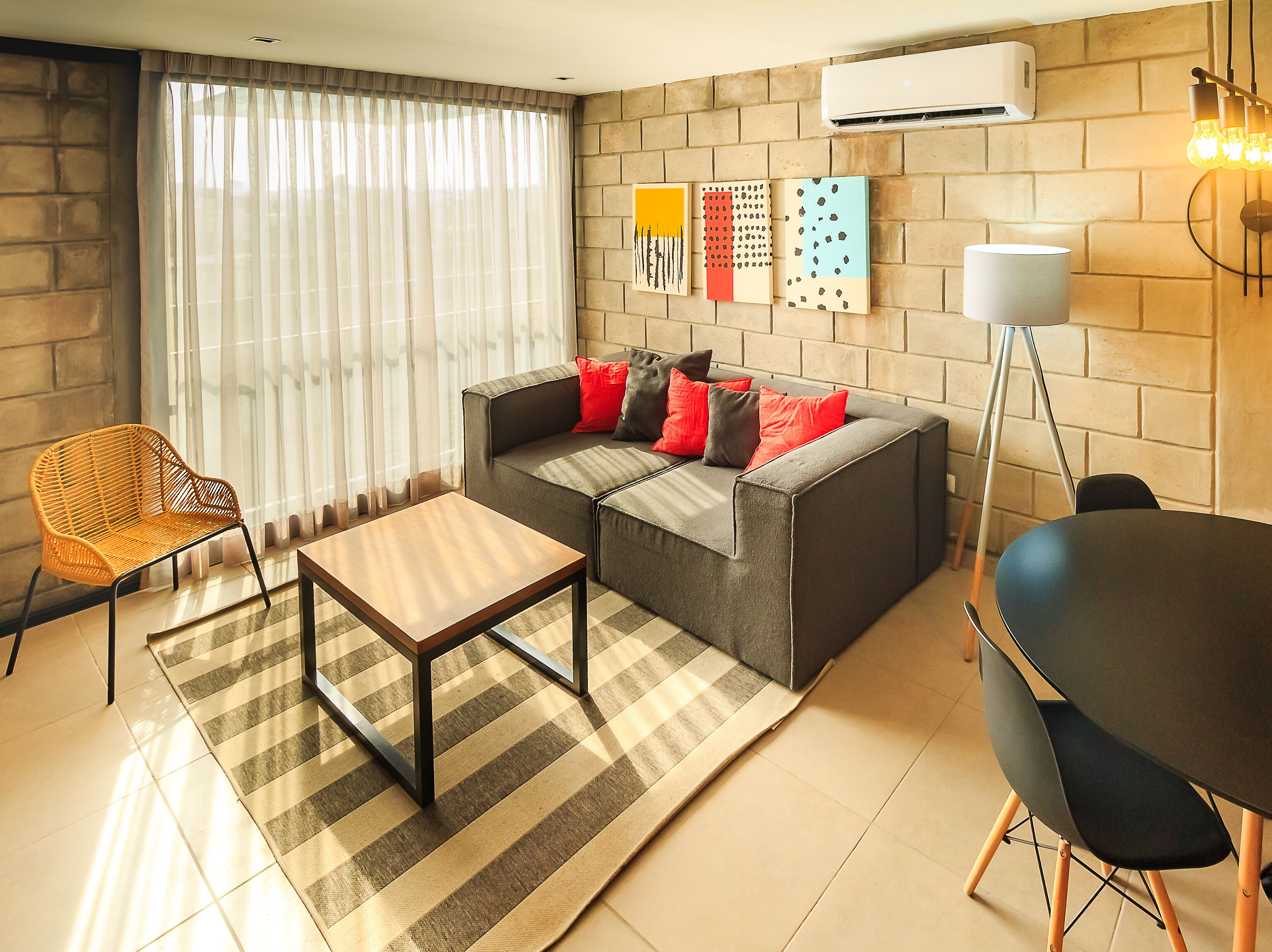 Una sala de estar moderna con un sofá gris, una mesa de centro de madera, una silla de mimbre y una mesa de comedor con sillas.
