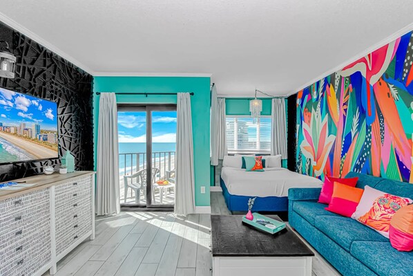 Une chambre avec un lit, un canapé, une télévision et un balcon offrant une vue sur la ville.