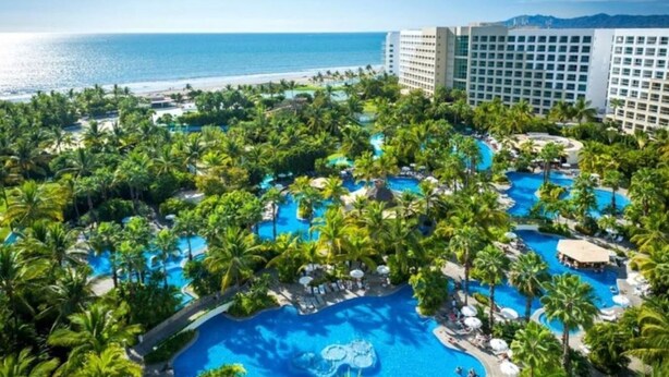 Un complexe hôtelier doté de plusieurs piscines, entouré de palmiers et offrant une vue sur la plage.