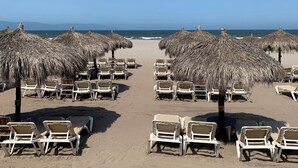 Une plage bordée de rangées de chaises longues et d’ombrelles en chaume, qui s’étend jusqu’à la mer.