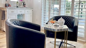 A modern living room with a black leather sofa, a small side table, and a large window with blinds.