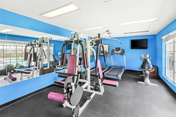 Une salle de sport équipée de divers appareils d’exercice, d’un tapis de course et d’un mur recouvert de miroirs.
