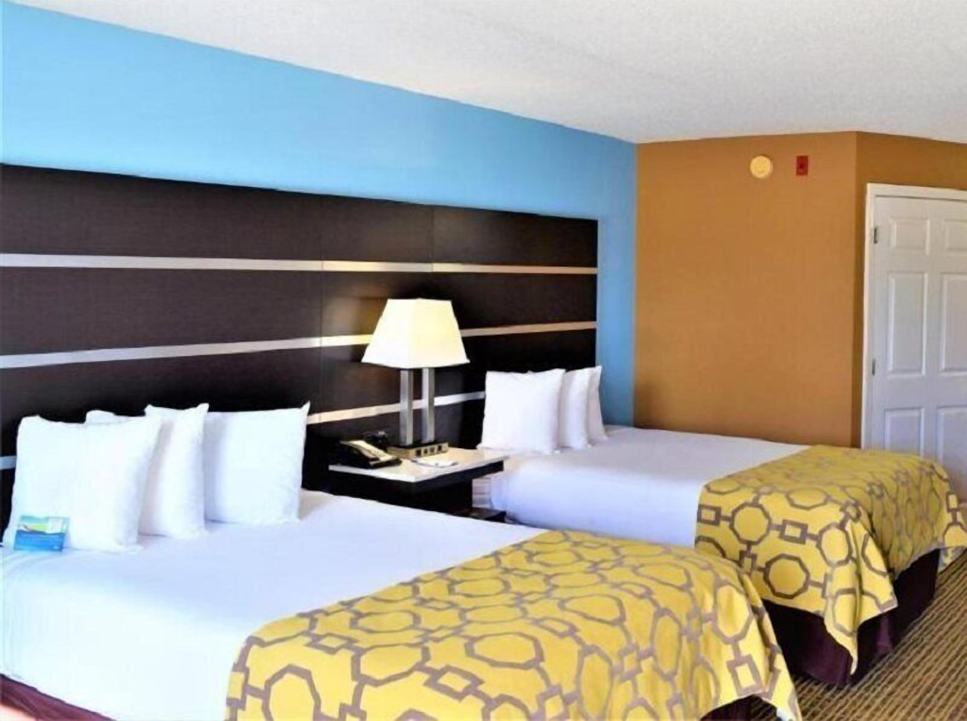 A hotel room with two beds, a nightstand with a lamp, and a door.
