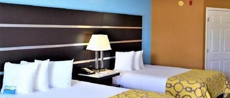 A hotel room with two beds, a nightstand with a lamp, and a door.