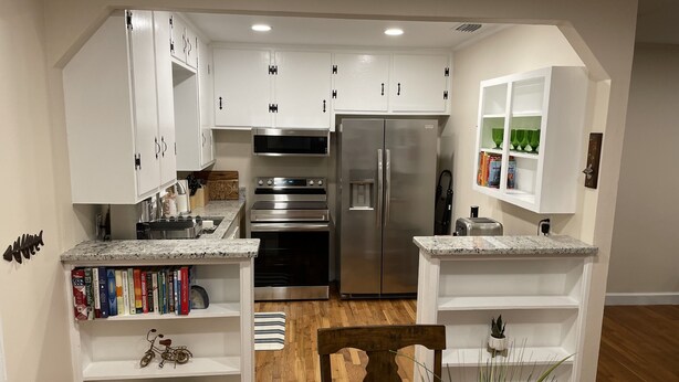 A modern kitchen with white cabinetry, stainless steel appliances, and a wooden dining table. - Enjoy Crawfordville at the Courtyard’s Pelican Cottage. (Crawfordville)