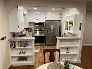 A modern kitchen with white cabinetry, stainless steel appliances, and a wooden dining table.