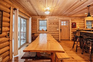 A log cabin interior with a long dining table, wooden benches, and a bar area. - Big Log Lodge by Taylor Made Deep Creek (McHenry)
