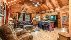 Interior de uma cabana de troncos com sala de estar, cozinha e espaço de bar.