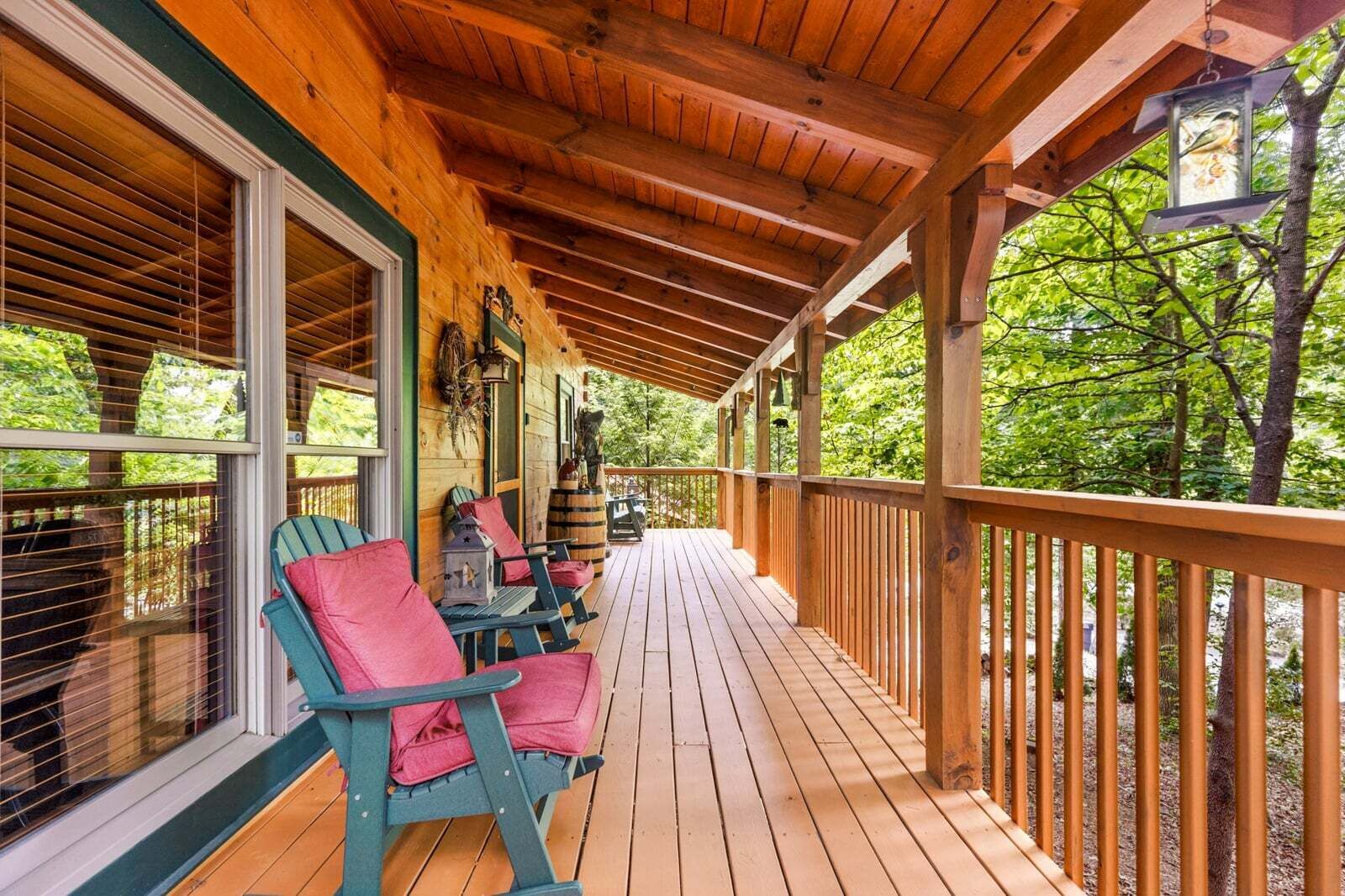 A wooden deck with chairs and a table, surrounded by a wooden railing, overlooking a forested area.