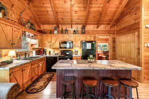 A wooden cabin interior with a kitchen featuring a large island, bar stools, and a dining area.