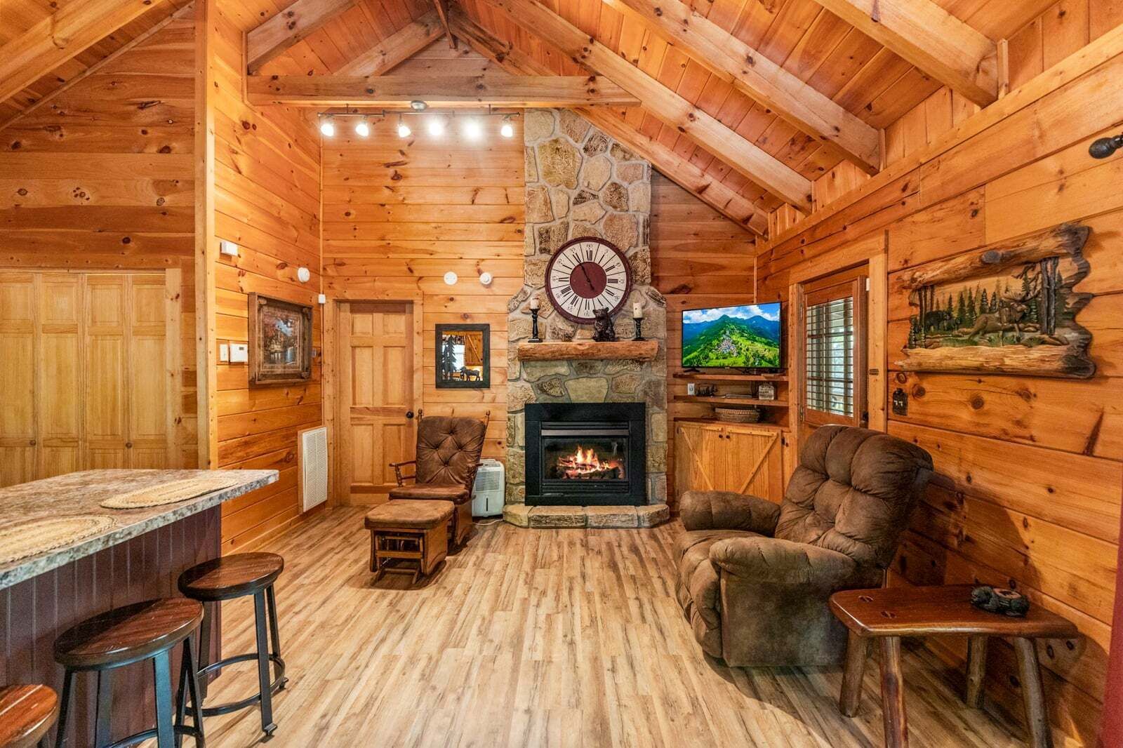 A log cabin interior with a stone fireplace, wooden walls, a mounted clock, and a television.