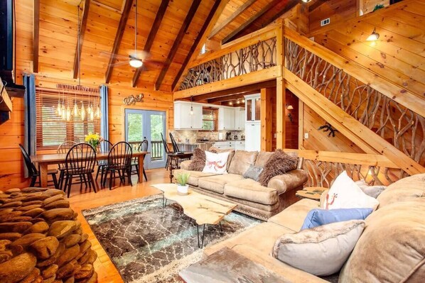 A cozy cabin interior with a dining area, kitchen, and living room. - Cherry Log Cabin | Hot Tub, Arcade & Pool Table (Cherry Log)