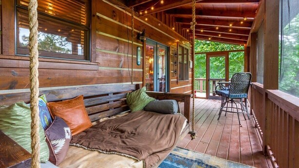 Una cabaña de madera con una cama acogedora, una hamaca y un porche con una silla.
