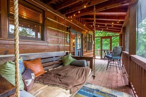 A wooden cabin with a cozy bed, a swing, and a porch with a chair. - Cherry Log Cabin | Hot Tub, Arcade & Pool Table (Cherry Log)