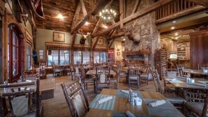 Un comedor rústico con mesas y sillas de madera, paredes de piedra y un candelabro.