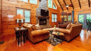 Un acogedor interior de cabaña de madera con chimenea de piedra, muebles de madera y ventanas amplias.