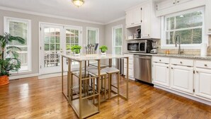 Una cocina con armarios blancos, un microondas de acero inoxidable y piso de madera.