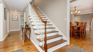 Una escalera de madera con balaustres blancos que conduce a un comedor con una araña.