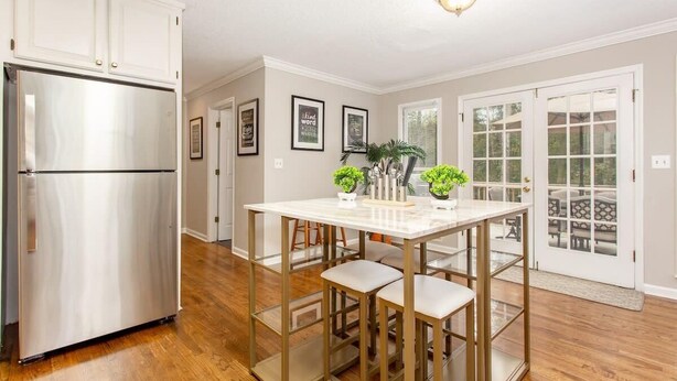 Una cocina con un refrigerador de acero inoxidable, una isla de mármol blanco con taburetes de bar y un comedor con vistas a través de puertas de vidrio.