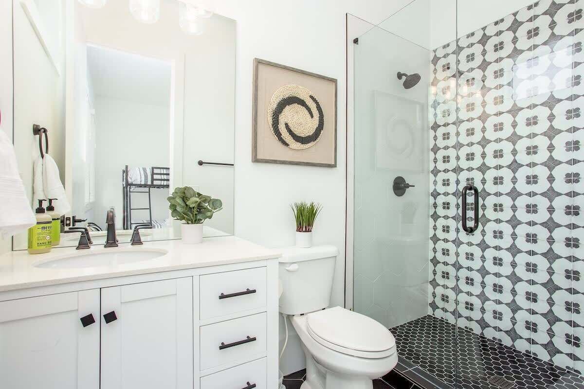 Une salle de bain moderne avec un meuble-lavabo blanc, une douche en verre et un mur recouvert de carreaux à motifs.