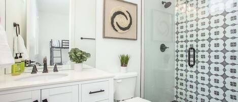 Une salle de bain moderne avec un meuble-lavabo blanc, une douche en verre et un mur recouvert de carreaux à motifs.
