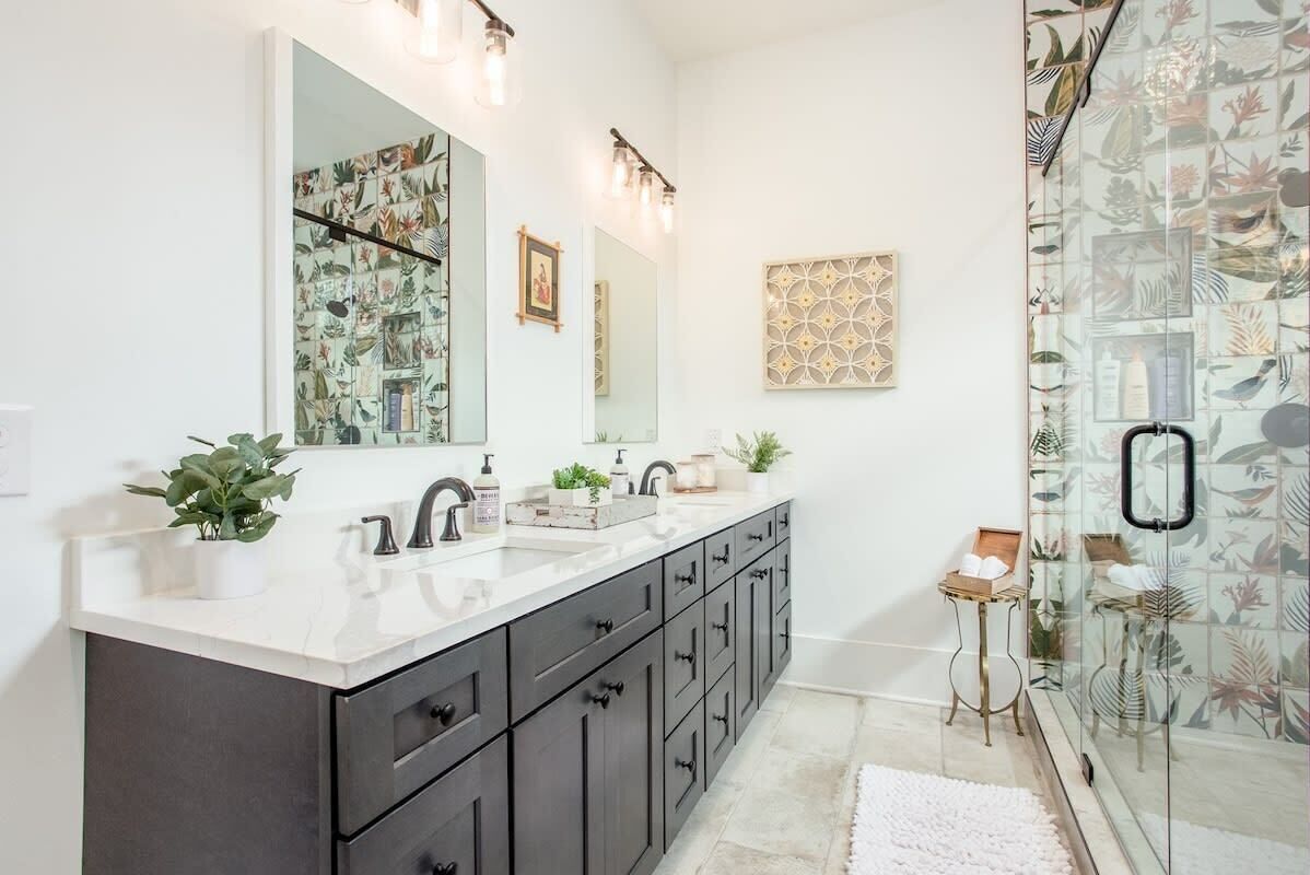 Un baño moderno con un espejo grande, lavamanos dobles, muebles oscuros y una zona de ducha con puerta de cristal.