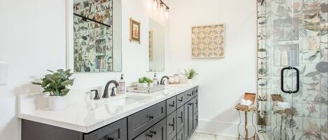 Un baño moderno con un espejo grande, lavamanos dobles, muebles oscuros y una zona de ducha con puerta de cristal.