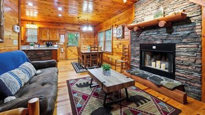 A cozy log cabin interior with a stone fireplace, wooden furniture, and a dining area. - New Hot Tub Grt WIFI Pool Table Sleeps10 Family (Blue Ridge)