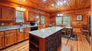 A wooden cabin interior with a kitchen, dining area, and a stone fireplace. - New Hot Tub Grt WIFI Pool Table Sleeps10 Family (Blue Ridge)