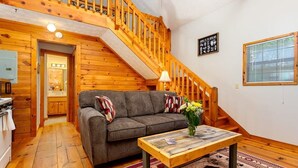 A cozy room with a wooden staircase, a sofa with pillows, a coffee table, and a rug.