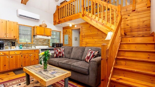 A cozy cabin interior with a wooden staircase, a sofa, a coffee table, and a kitchen area.