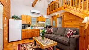 A cozy cabin interior with a wooden interior, a kitchen with wooden cabinets, a sofa, and a dining table.