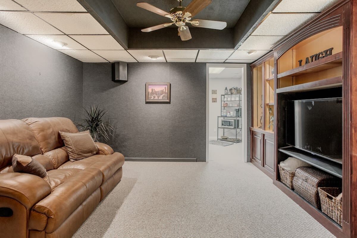 A living room with a leather couch, a ceiling fan, a framed picture on the wall, and a TV on the right.