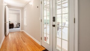 A hallway with wooden flooring, a white door with glass panels, and a view of an outdoor patio area. - Hidden Gem Retreat | 2BR Basement |Near Mall of GA (Buford)