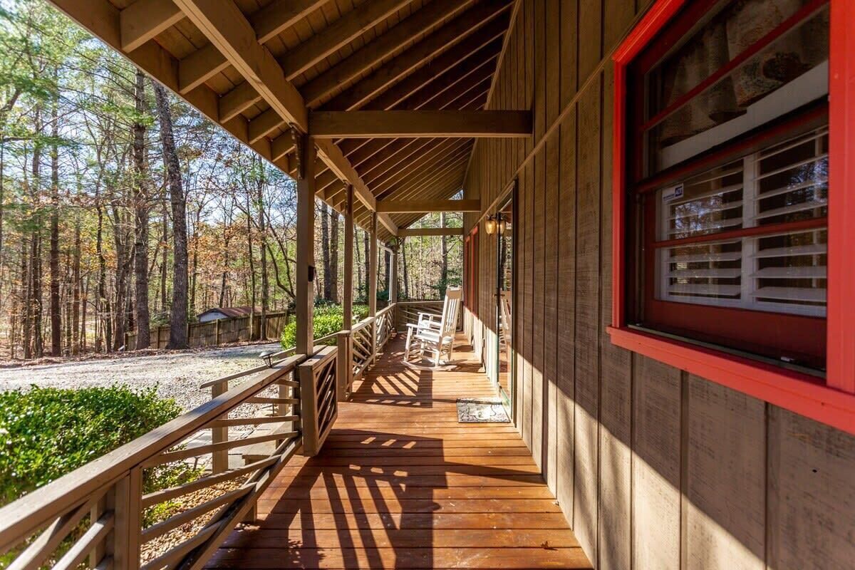 A covered wooden deck with a railing, overlooking a forested area.