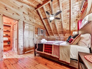 Quarto de cabana de tronco com uma cama, um ventilador de teto, paredes de madeira e piso de madeira.