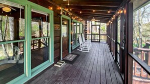 Een houten veranda met schommelstoelen, lichtjes en grote ramen.