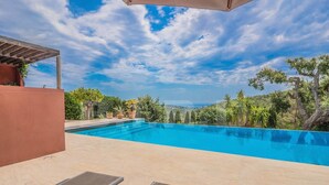 Una piscina con sillas de descanso, una pérgola y vistas a un paisaje montañoso.