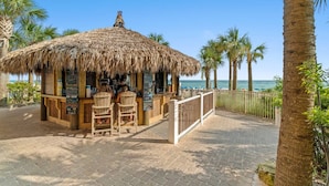 A beachside bar with a thatched roof, wooden chairs, and a view of the ocean. - Calypso Resorts Tower III Unit 310 (Panama City Beach)