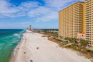 A beachfront hotel with a long sandy beach, a pier, and a clear blue sky. - Calypso Resorts Tower III Unit 310 (Panama City Beach)