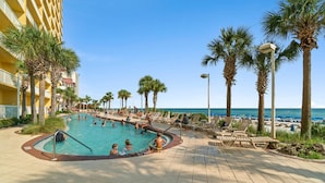 A pool area with lounge chairs and palm trees, overlooking a beach. - Calypso Resorts Tower III Unit 310 (Panama City Beach)