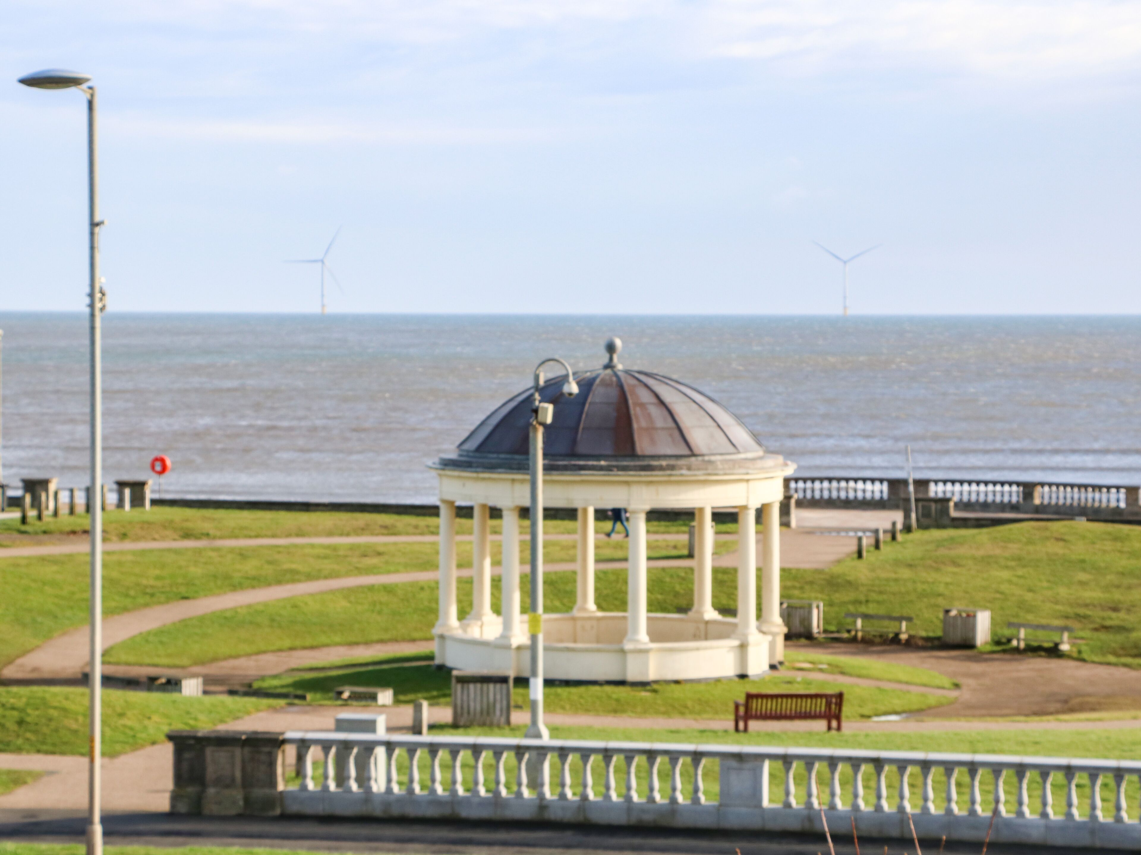 A gazebo with a dome roof, surrounded by a grassy area and a paved walkway.