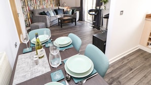 A dining area with a table set for two, a sofa in the background, and a colorful wall.