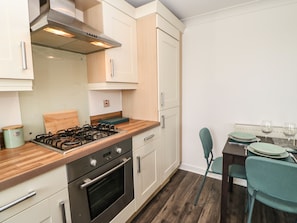 A modern kitchen with a gas stove, oven, and wooden countertop. There is a dining area with a table and chairs. - Sandy Corner (Blyth)